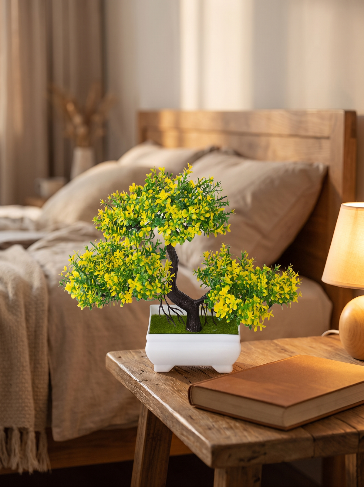 Faux blossom bonsai tree on a bedside table beside a book and a lamp