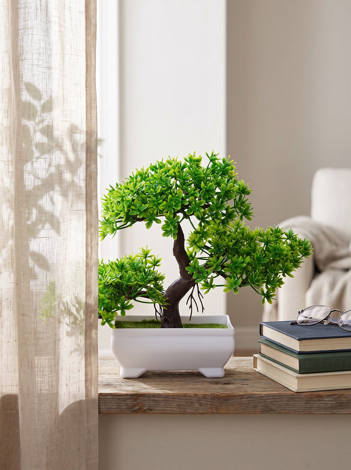 Faux green bonsai tree on a windowsill beside a stack of books